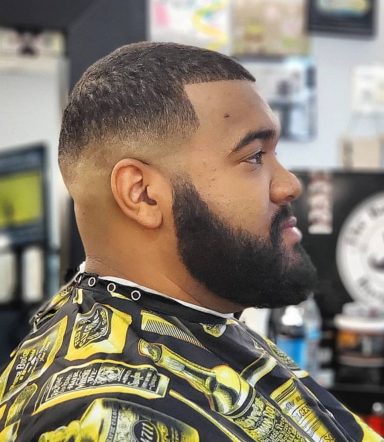 Man with a beard and a faded haircut, sitting in a barbershop chair.