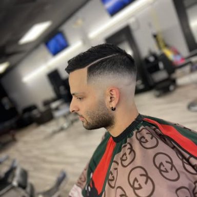 Man with a stylish fade haircut and sharp line, wearing a barber cape.