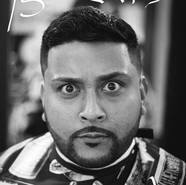A surprised man with a neatly styled beard, wearing a barber's cape.