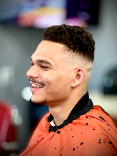 Young man with a stylish haircut smiling in a barbershop setting.