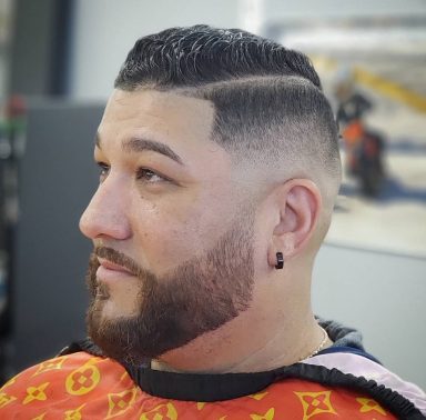 Man with a neatly styled haircut and beard, sitting in a barbershop.