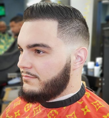 Man with a neatly styled haircut and a full beard, wearing a patterned barber cape.