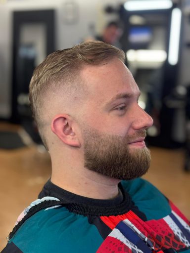 Man with short hair and beard, smiling in a barbershop setting.