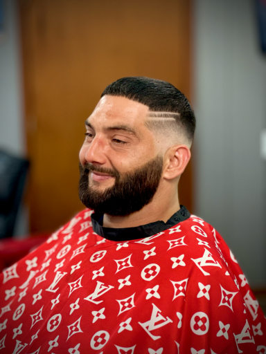 Man with a beard smiling, wearing a red haircut cape with a logo pattern.