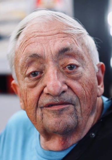 Elderly man with gray hair and glasses, looking directly at the camera.