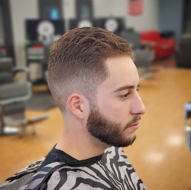 Young man with a fade haircut and beard, sitting in a barber shop.