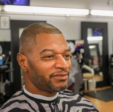 Man with a short haircut and beard, smiling in a barbershop setting.