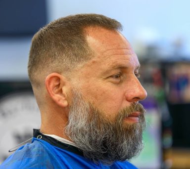Profile of a man with a short beard and neatly styled hair, wearing a blue shirt.