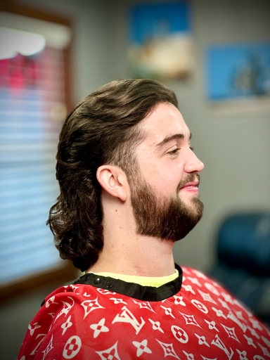 Young man with a mullet hairstyle, smiling, sitting in a barber's chair.