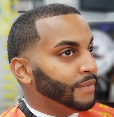 Close-up of a man with a well-groomed beard and short hair in a barbershop.