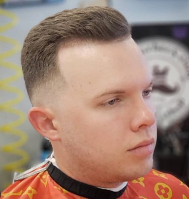 Young man with a fade haircut, wearing a barber cape, looking thoughtfully.