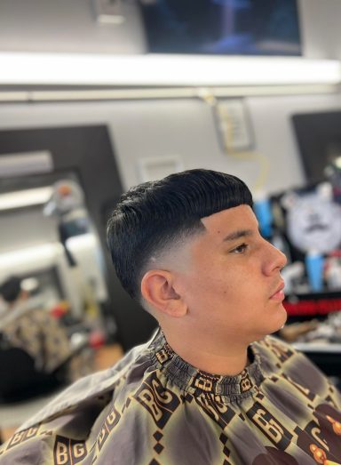 Young man with a fade haircut, wearing a patterned shirt, seated in a barbershop.
