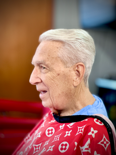 Elderly man with white hair smiling, wearing a red patterned shawl.