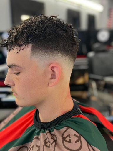 Man with curly hair and a fade haircut, sitting in a barbershop chair.