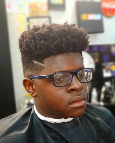 Young man with a stylish haircut and glasses, sitting in a barbershop chair.