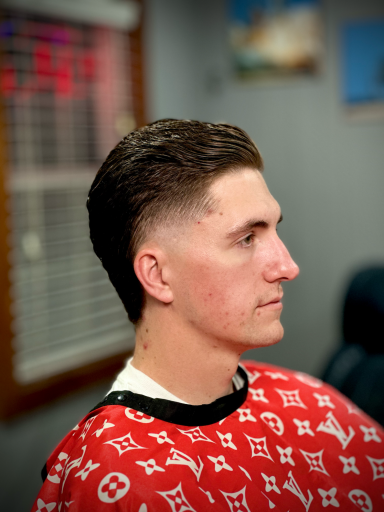 Young man with a buzz cut and fade, sitting in a barbershop chair, wearing a patterned cape.
